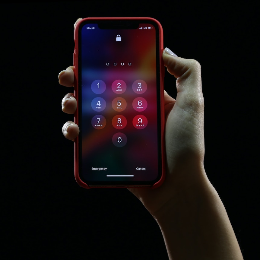 A hand holding an iPhone against a black background. The phone is asking for the user's passcode.