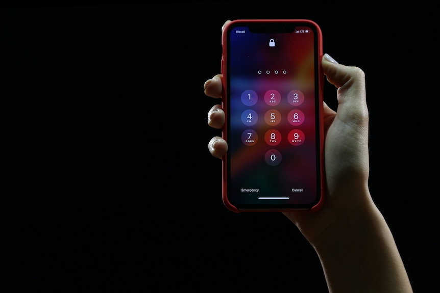 A hand holding an iPhone against a black background. The phone is asking for the user's passcode.