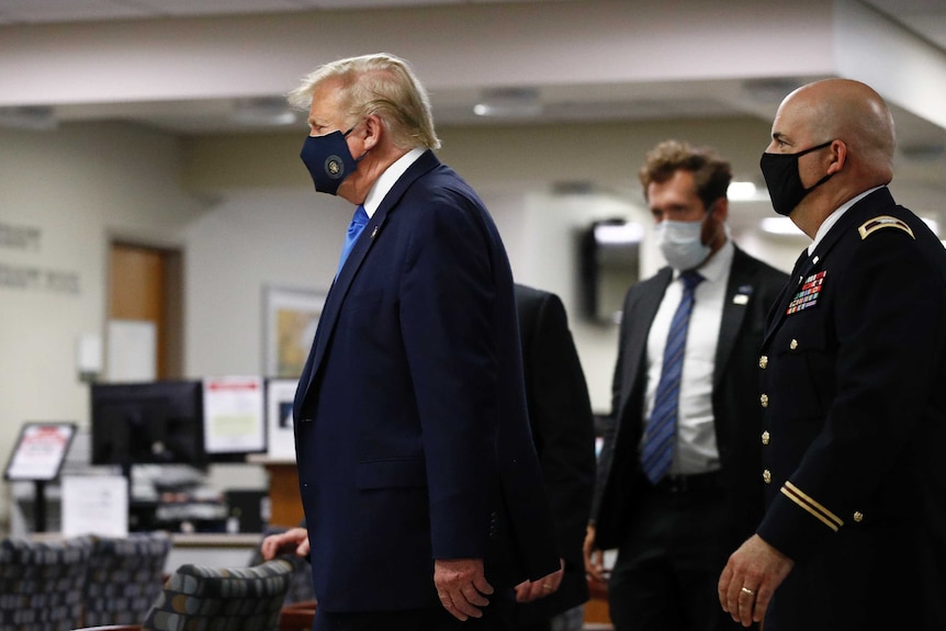 President Donald Trump and several men behind him wear black face masks as they walk down a hallway.