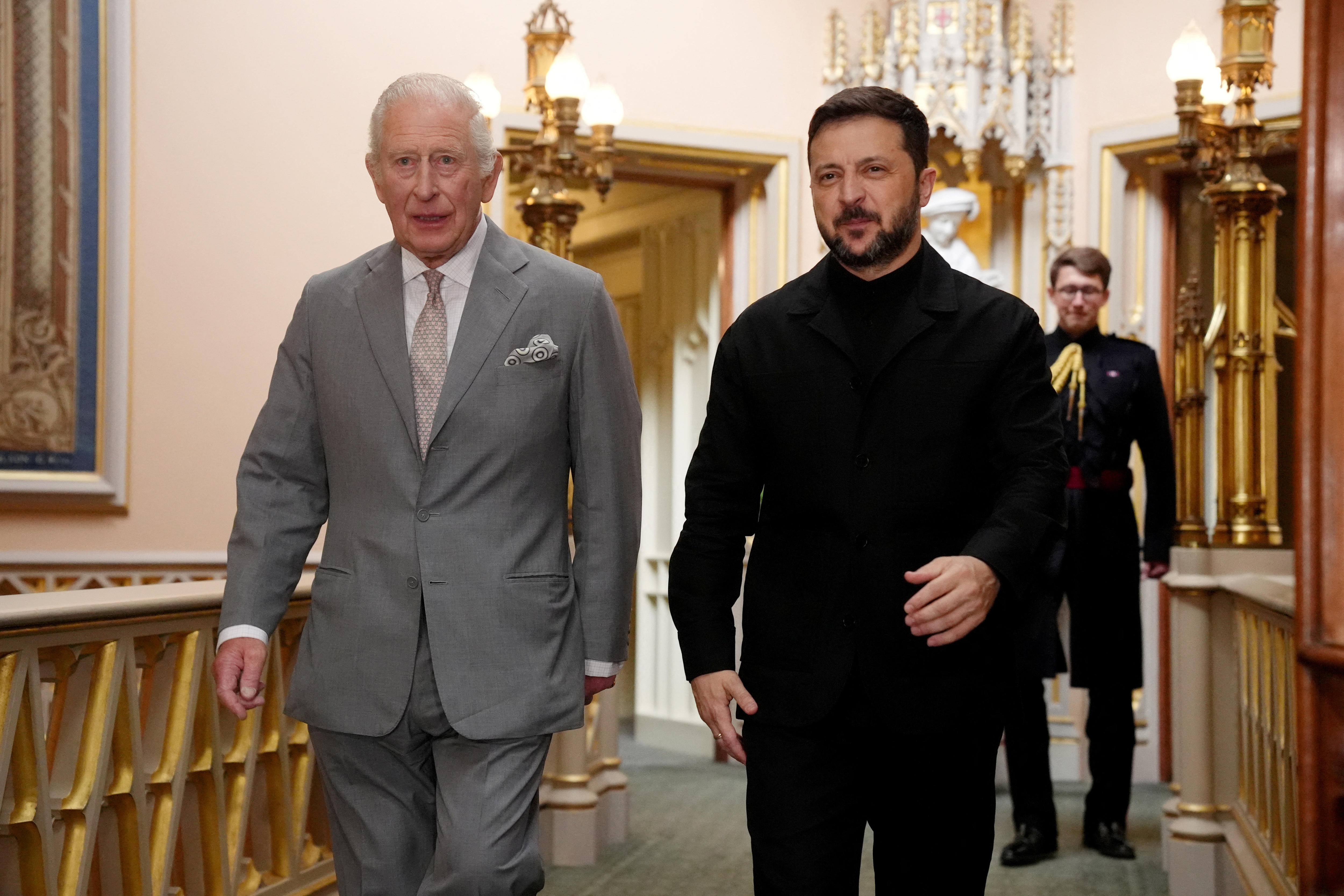 Volodymyr Zelenskyy and King Charles walking side by side through a hallway in Windsor Castle.