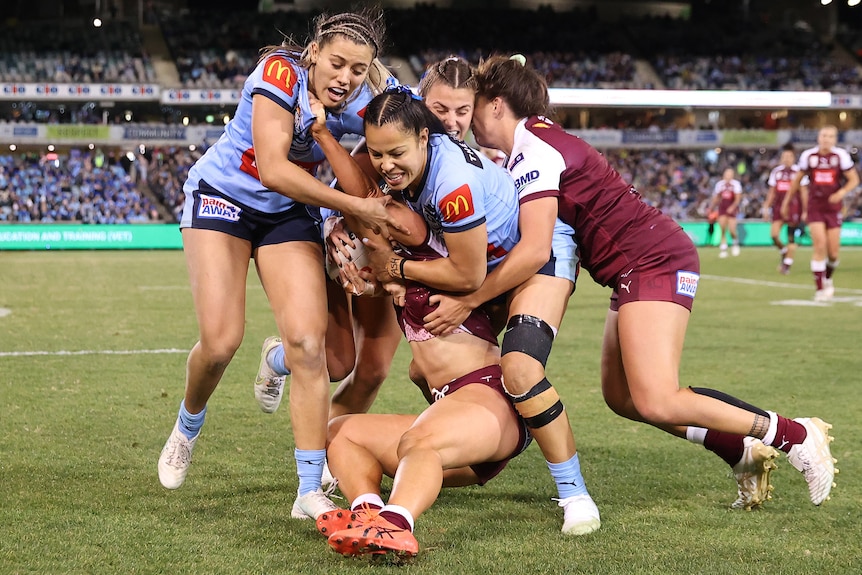 NSW Women's State of Origin players gang tackle Queensland's Emily Bass.