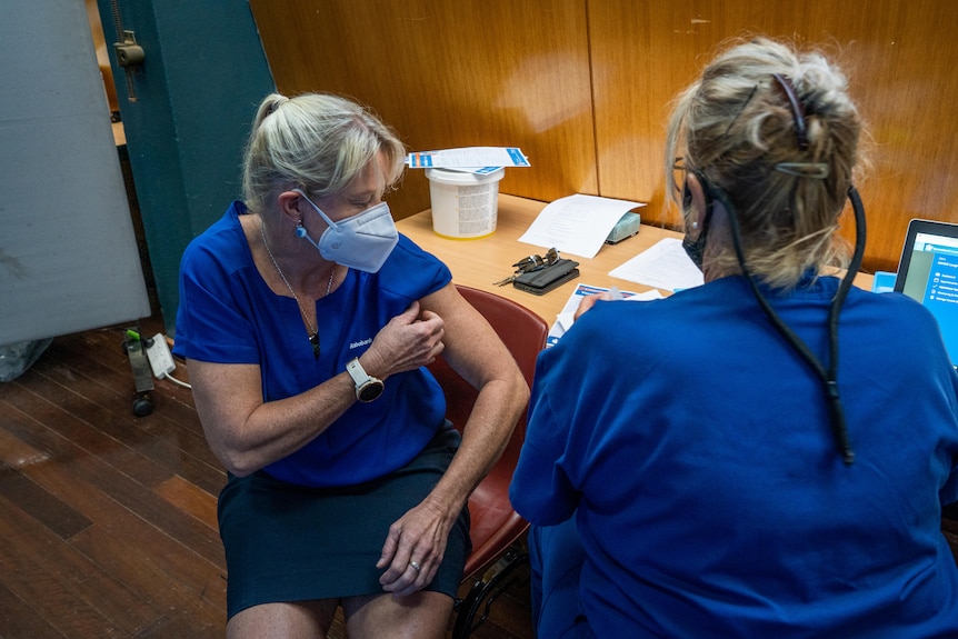 A woman in a mask rolls up her sleeve to get vaccinated.