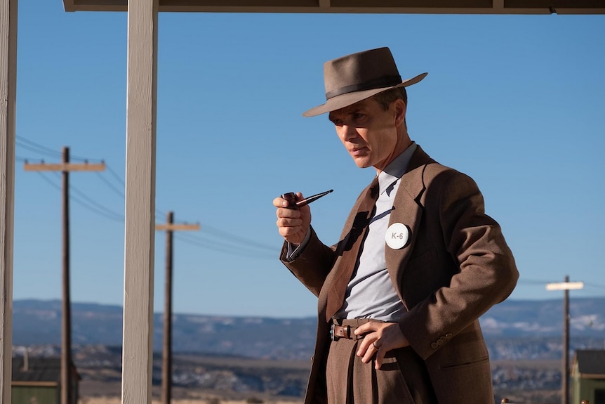 A still from the film Oppenheimer, showing Cillian Murphy as Robert Oppenheimer standing near power lines.