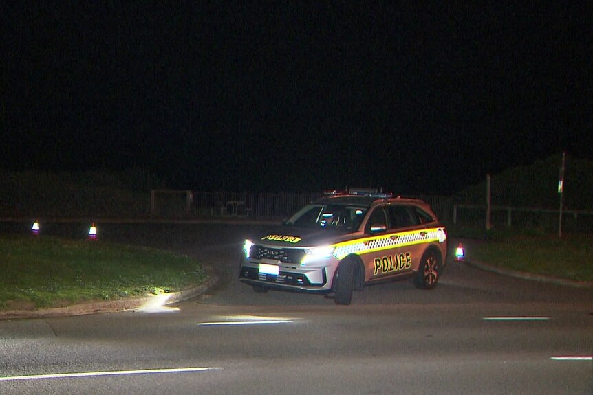 A police car at the entrance to a car park at night