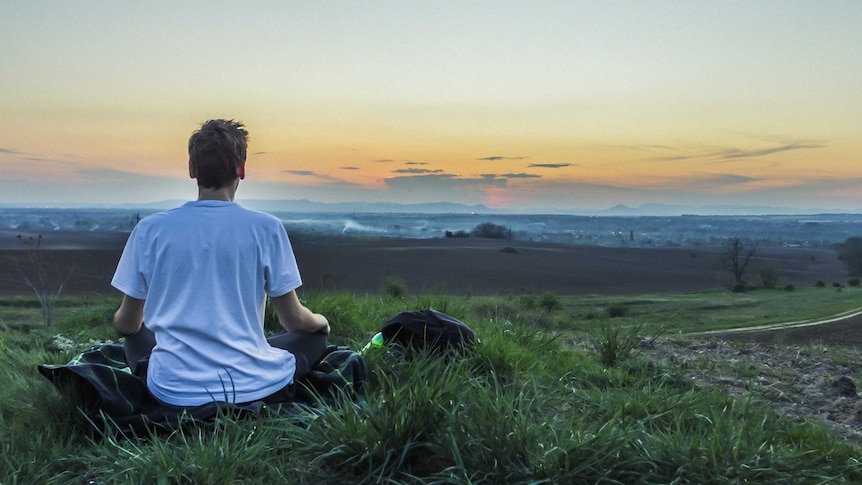 Man meditating in a grassy area for a story about hoe to silence the inner critic