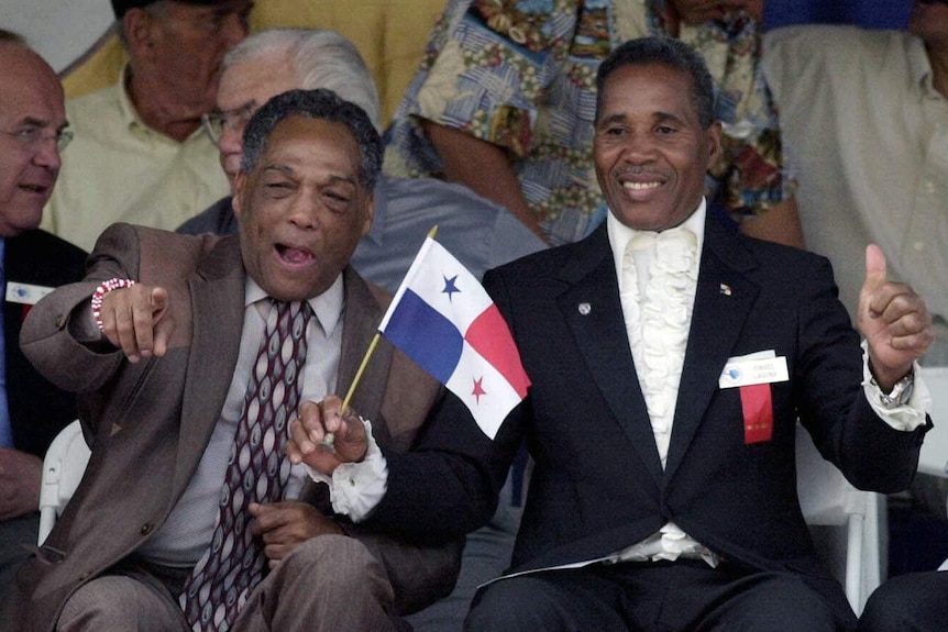 Two men smile, point and give thumbs up as one waves a Panama flag.