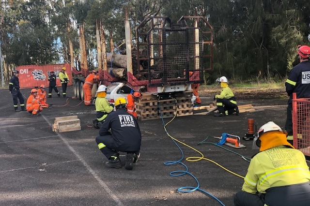 MFS and other emergency workers gather around a fire-affected logging truck in an emergency scenario.