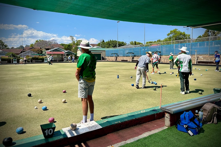 A few people stand on a green playing lawn bowls