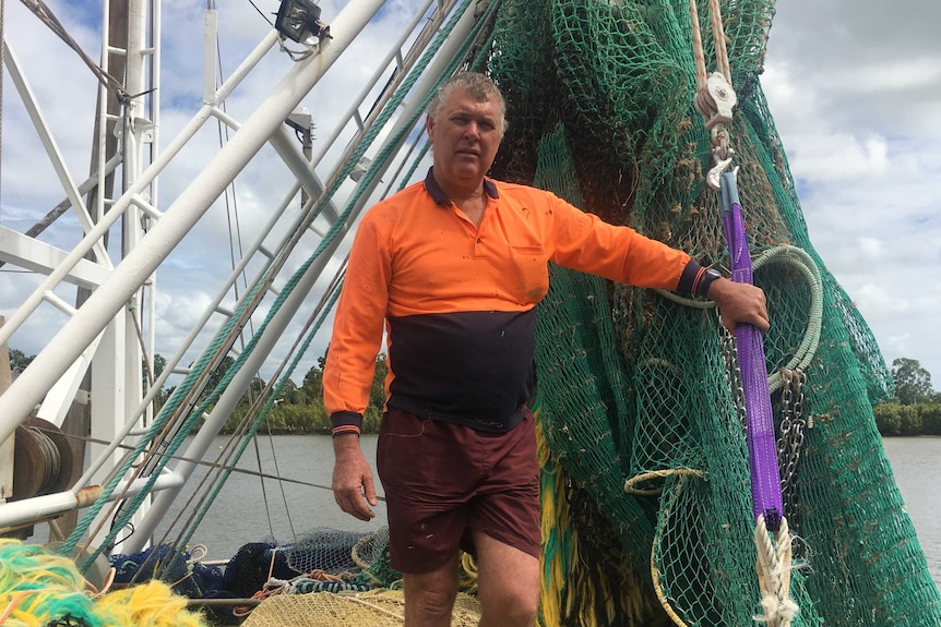 A middle aged man holds onto his trawler nets on top of his boat; he appears frustrated.