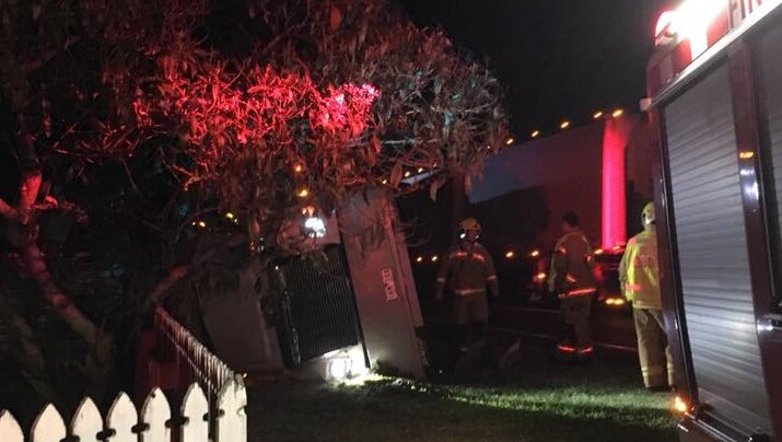 A truck on its side near a fence at night with firefighters around