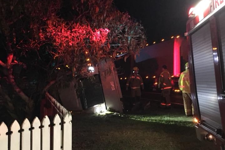 A truck on its side near a fence at night with firefighters around