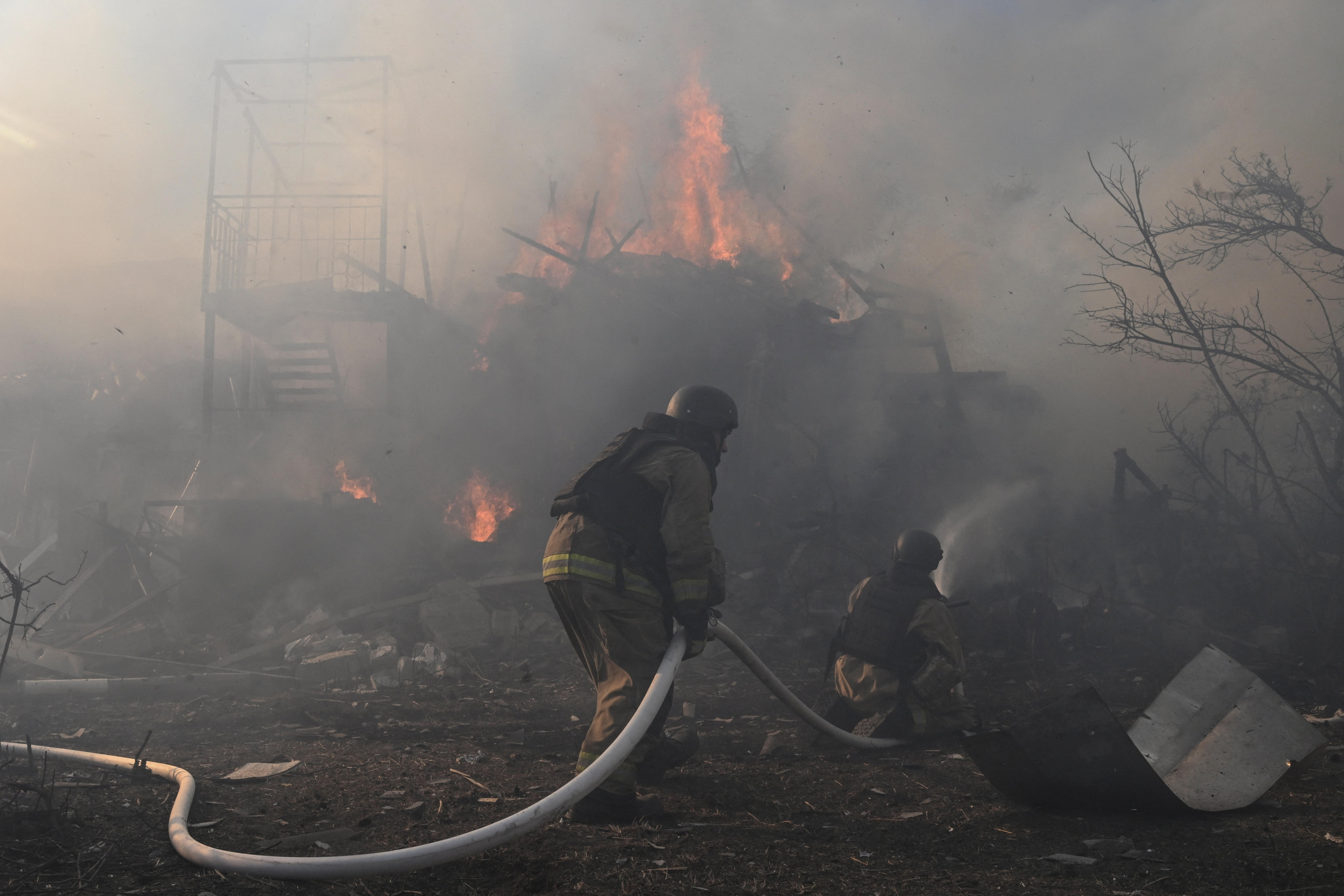 Firefighters work at the site of residential houses damaged by a Russian air strike. The house is burning and smoking.