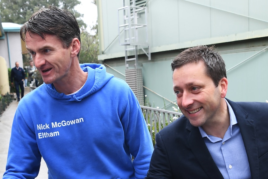 Nick McGowan, in a blue hoodie reading 'Nick McGowan Eltham' next to a smiling Matthew Guy in a suit, both reaching out hands.