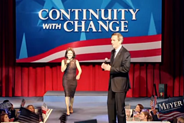 Julia Louis-Dreyfus, as Selina Meyer in Veep, walks onto a stage with the slogan Continuity With Change behind her.