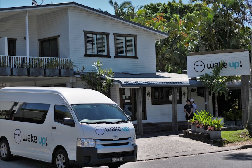 A white two storey building with a white van out the front, all with 'wake up!' signage