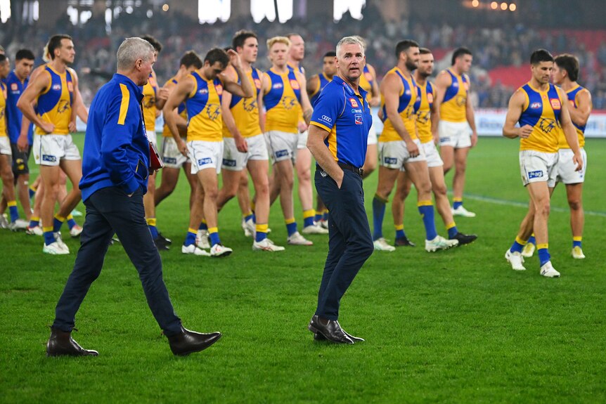 West Coast Eagles coach Adam Simpson walks on the ground near another coach and in front of his players.