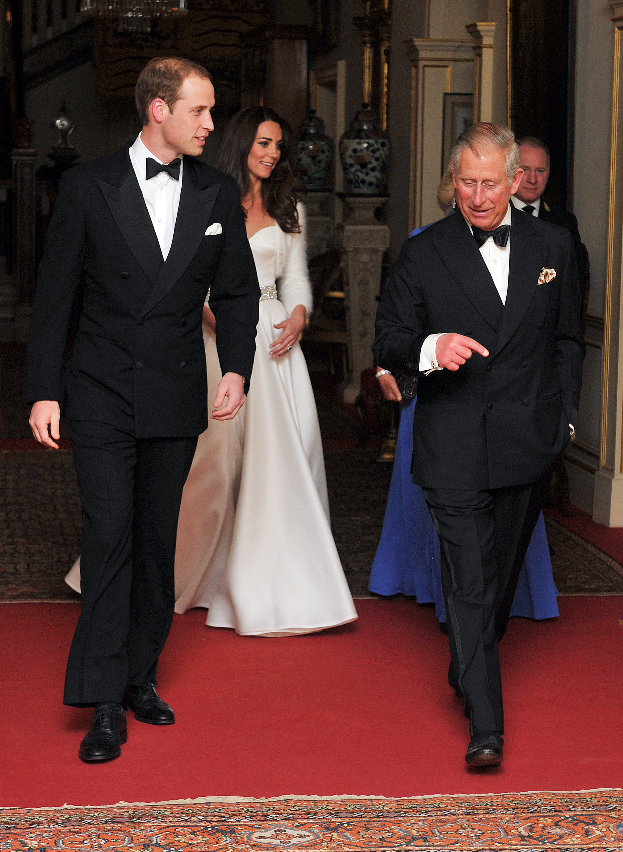 Prince William and Charles walk wearing black suits with bow ties while Kate wears a white gown