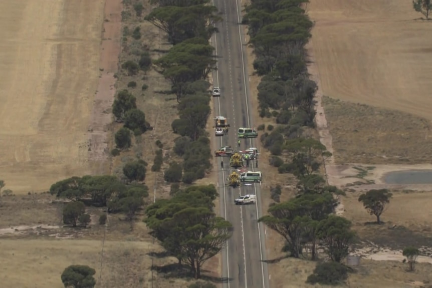 A series of emergency vehicles on a highway surrounded by fields