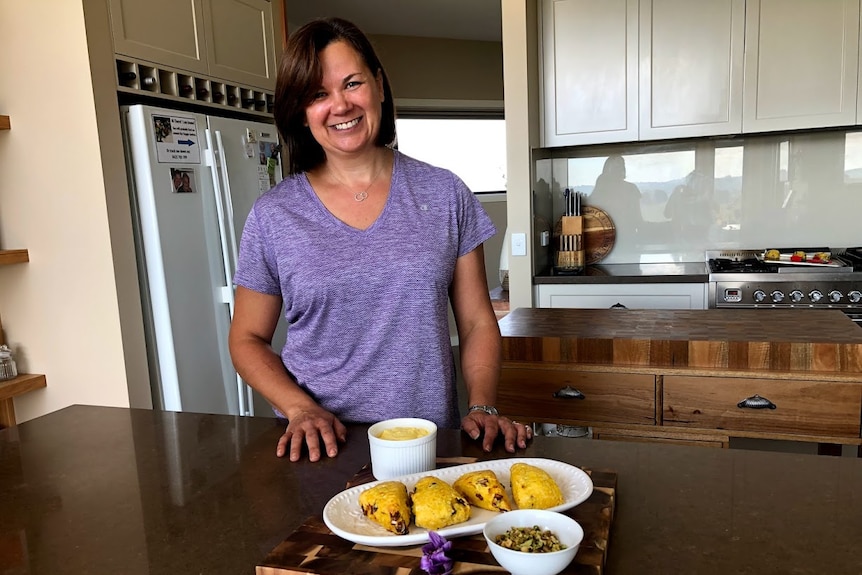 Woman standing in kitchen with board of scones and cream.