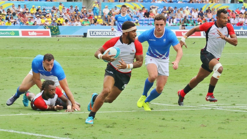 A PNG player runs toward camera with the ball, pursued by a Scottish player and backed up by a teammate on the right.
