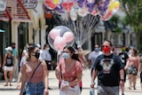 A woman holding a balloon wears a face mask as she walks through a busy pedestrian area in a theme park