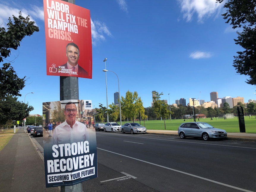 Two election posters on a stobie pole showing Peter Malinauskas and Steven Marshall. In the background is the city skyline