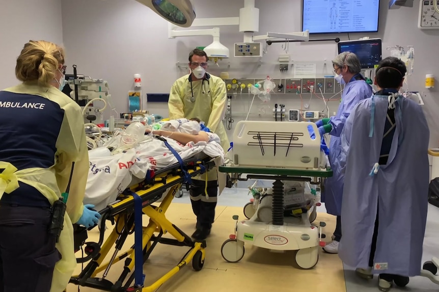 An ambulance officer wheels a COVID-19 patient into a treatment room. 