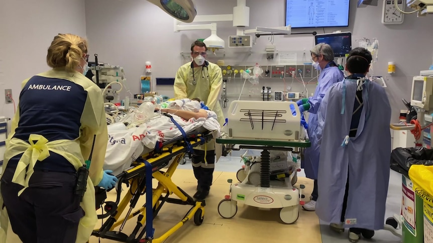 An ambulance officer wheels a COVID-19 patient into a treatment room. 