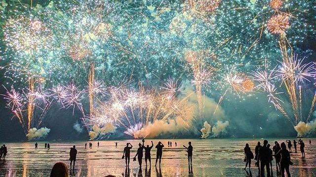Fireworks light up the sky and silhouettes of people watching