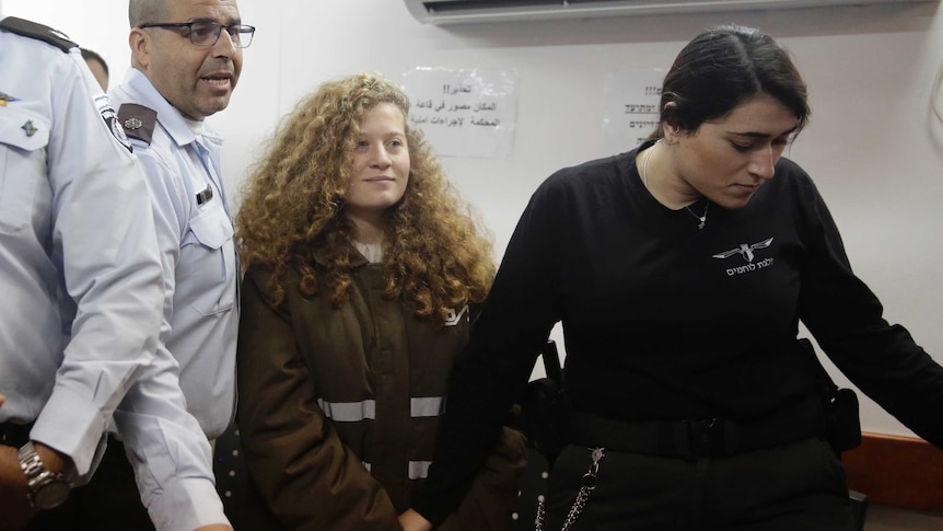 Wide shot of Ahed Tamimi standing in court flanked by guards.