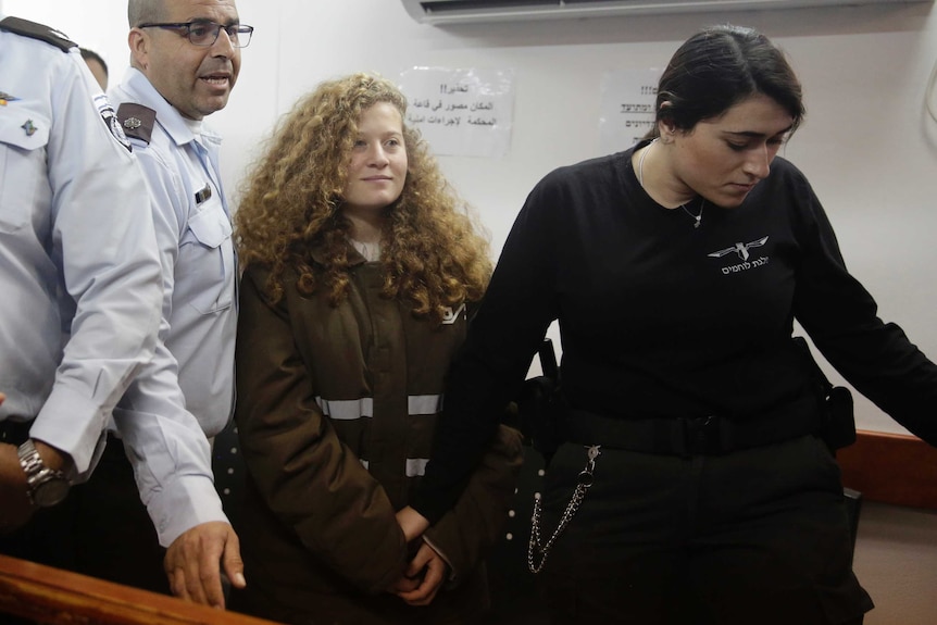 Wide shot of Ahed Tamimi standing in court flanked by guards.