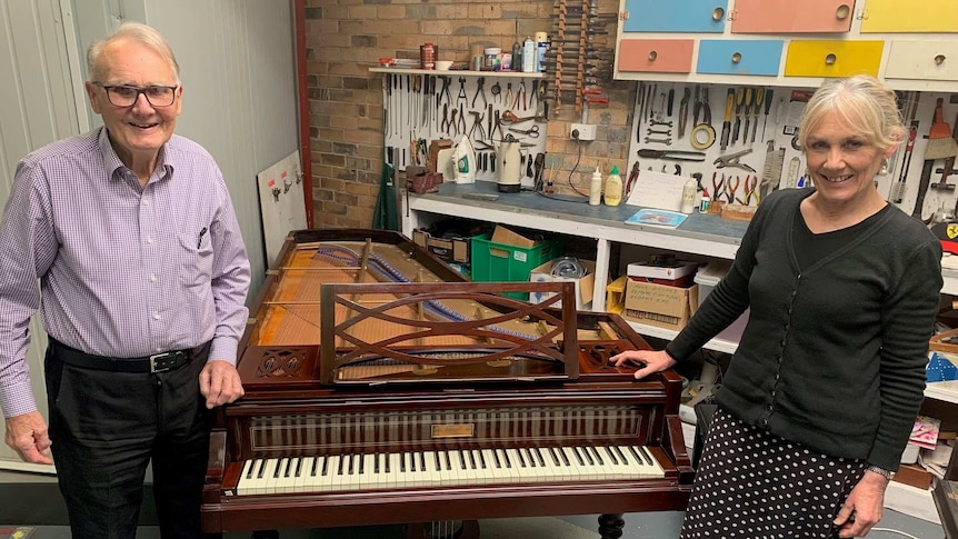 A man in his 80s and woman in her 50s stand on either side of a grand piano