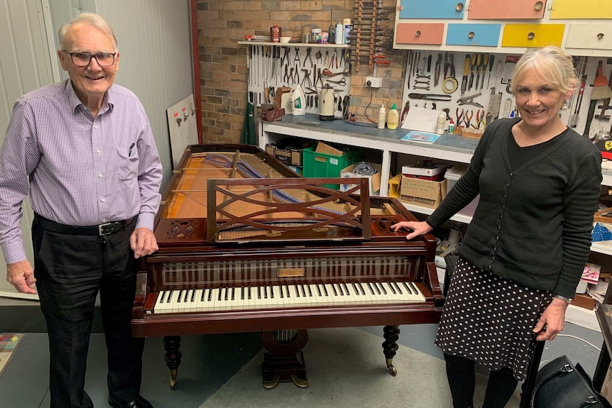 A man in his 80s and woman in her 50s stand on either side of a grand piano