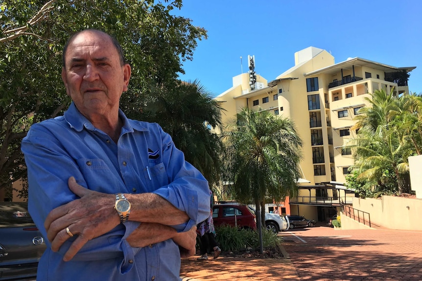 Dominic Fracaro. stands in front of a building with his arms crossed.