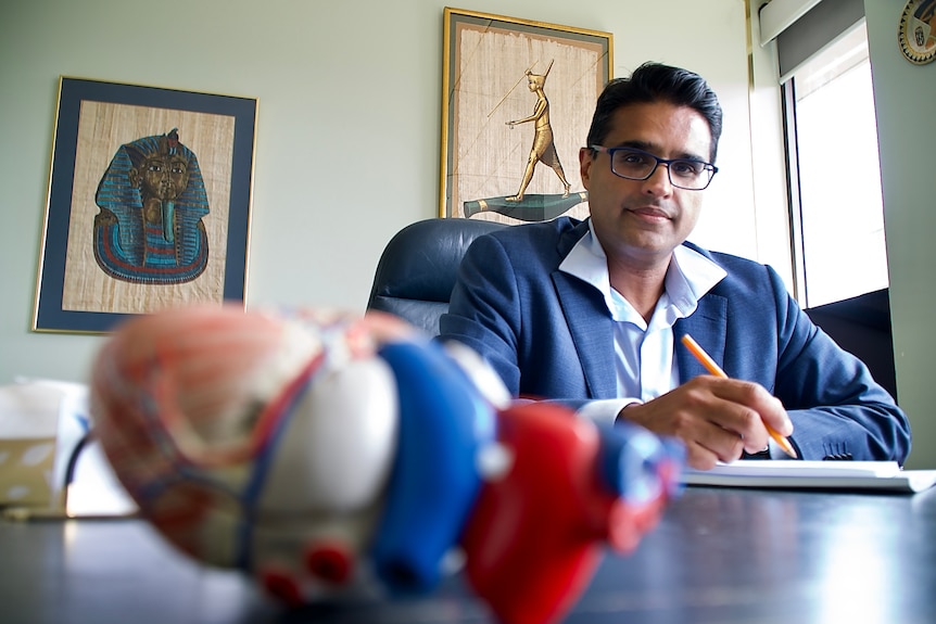 A doctor wearing a blue suit, sitting at a desk in an office