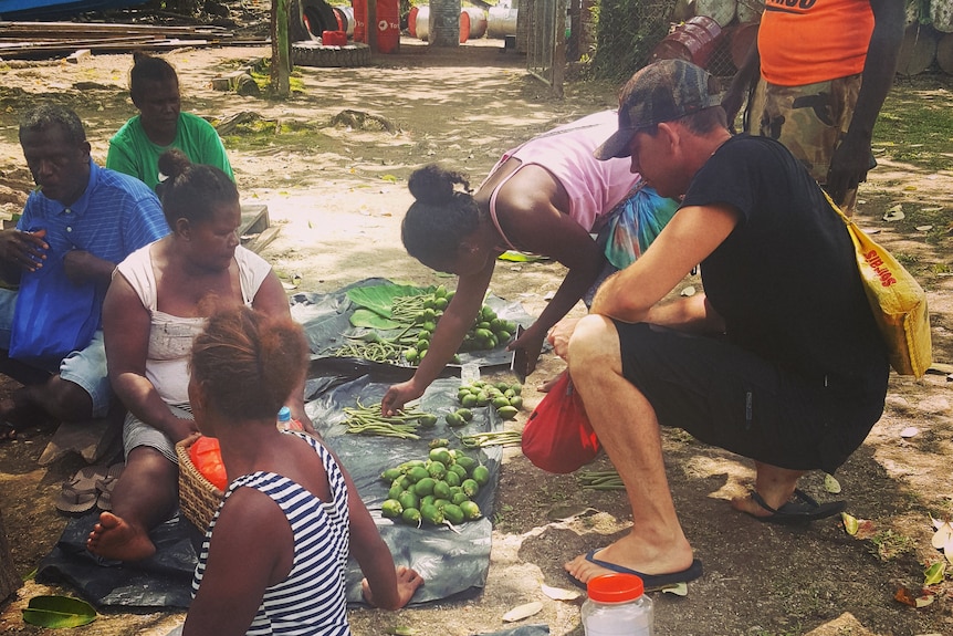 Trent Lee crouches among locals picking out fruit in the Solomon Islands