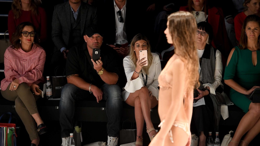 Guests take photographs with smartphones as a model walks the runway