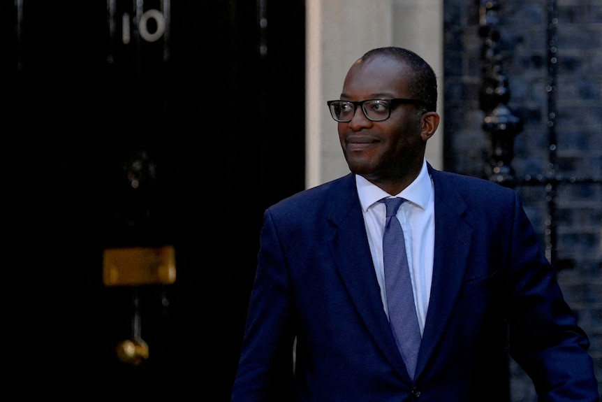Un homme noir portant un costume et une cravate se tient devant le numéro 10 Downing Street.