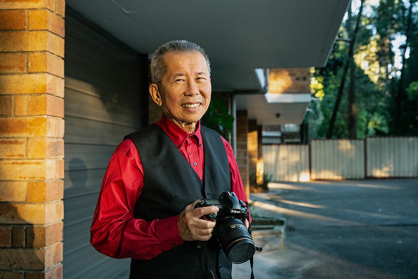 William, an older man, smiles while holding a professional camera