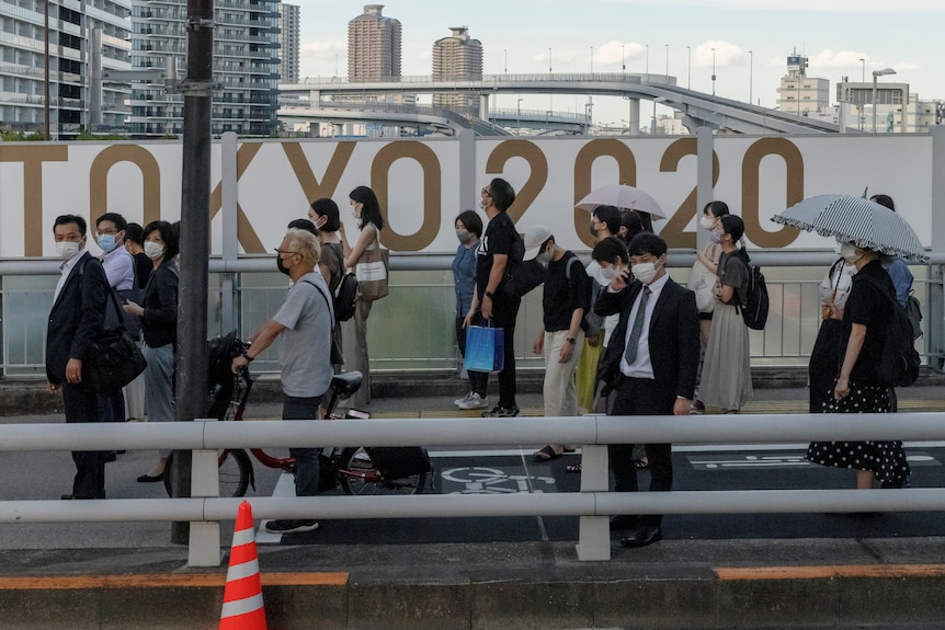 People wait for a train in front of Tokyo 2020 signage.