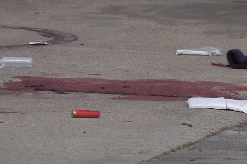 A pool of blood, bullet casings and bandages lie on a street.
