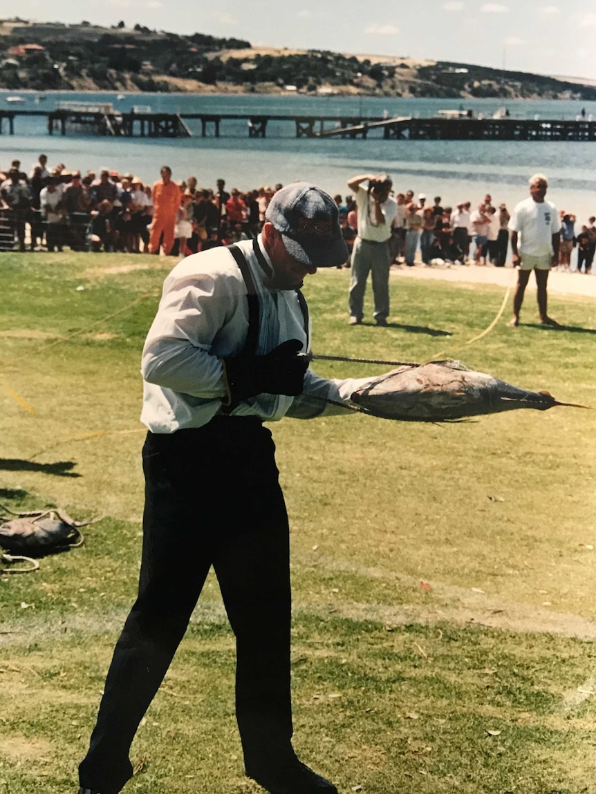 A man in a tuxedo and cap holds a tuna.