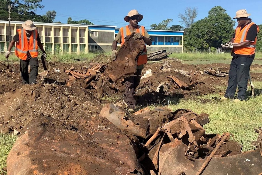 The UXO clearing team wearing hi-vis in a ground with plane debris.