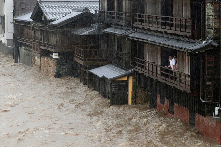 Two people watch a raging flood from their balcony