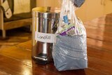 A bag of rubbish and a rubbish bin on a kitchen counter.