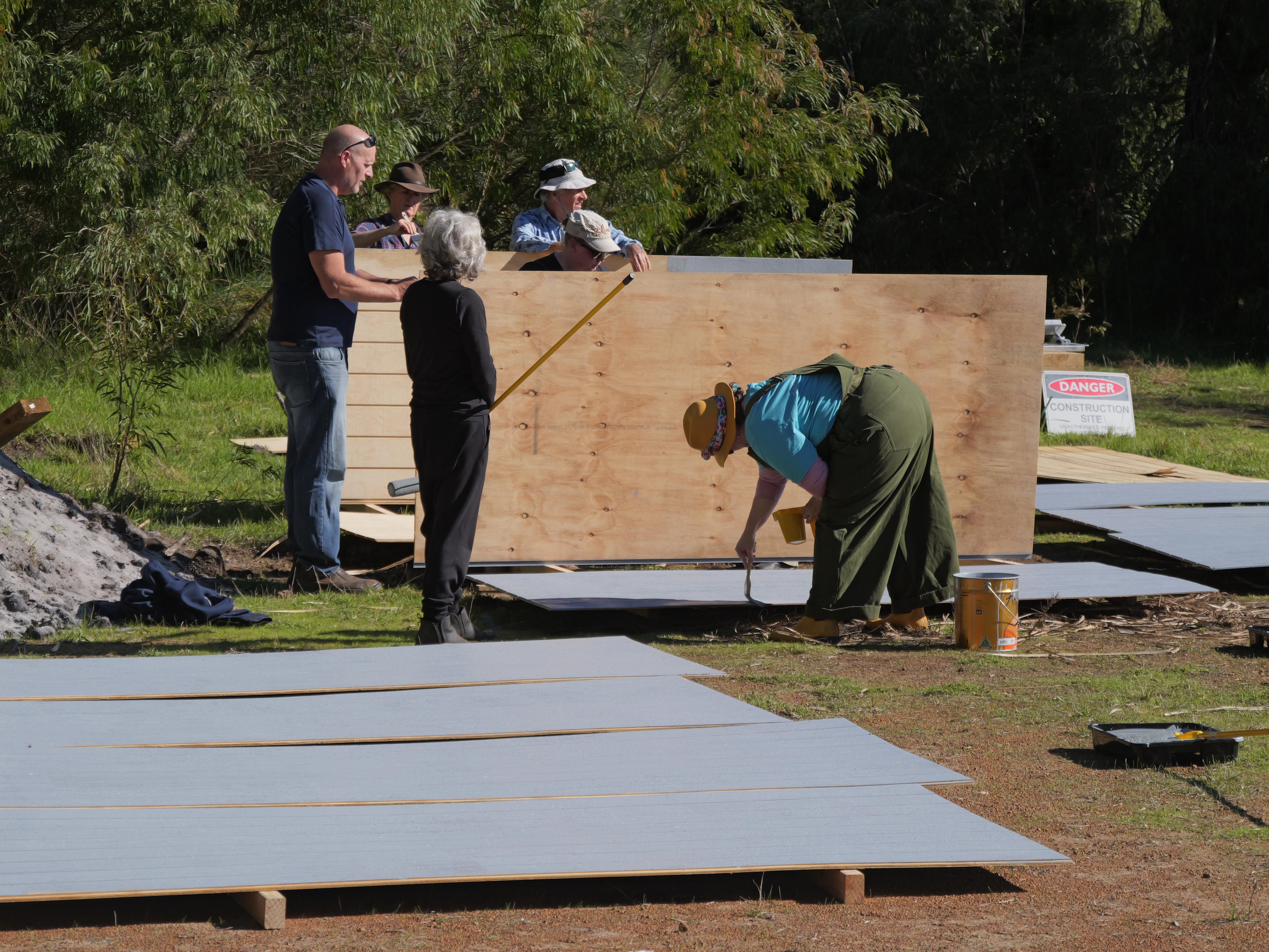 Four people paint wood panels and two people watch on.