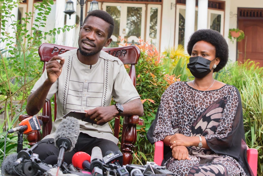 Uganda's leading opposition challenger Bobi Wine speaks to press as he sits next to his wife in an outdoor setting.