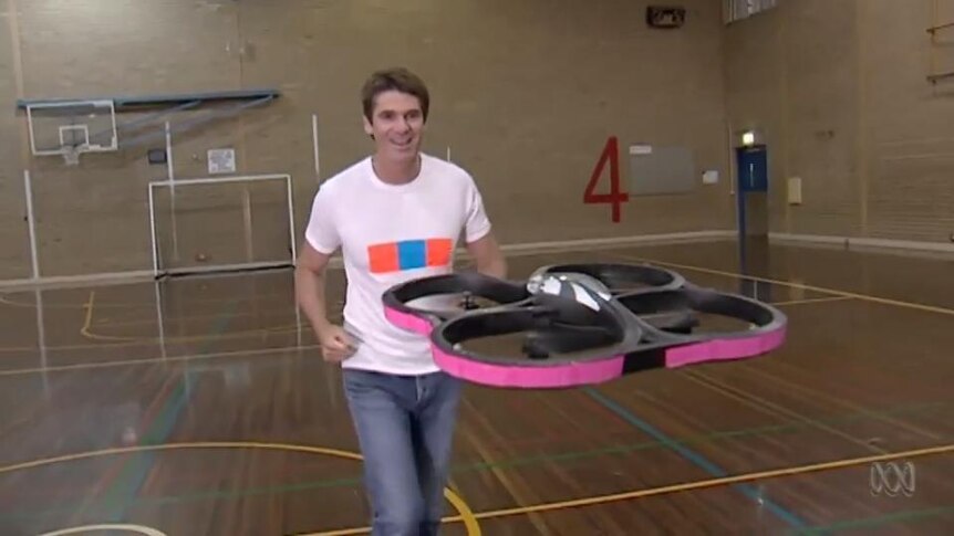 Presenter Graham Phillips runs after a hovering drone device in a gymnasium