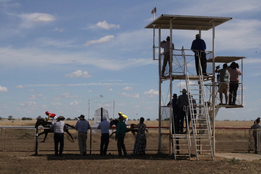 A group of people standing at a fence and in a tower watching horses cross the finish line of a race.