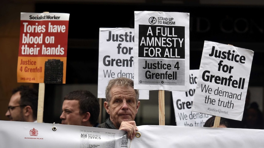 Demonstrators gather outside the Grenfell Tower public Inquiry holding signs.